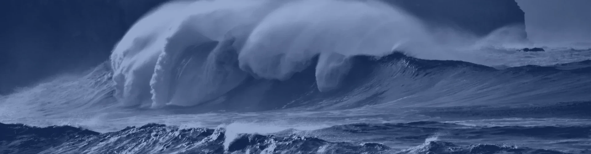 Tinted detail of a photo: Huge breaking wave with spray streaming back from its crest in front of dark cliffs topped by a house and telegraph poles, under a gloomy sky.